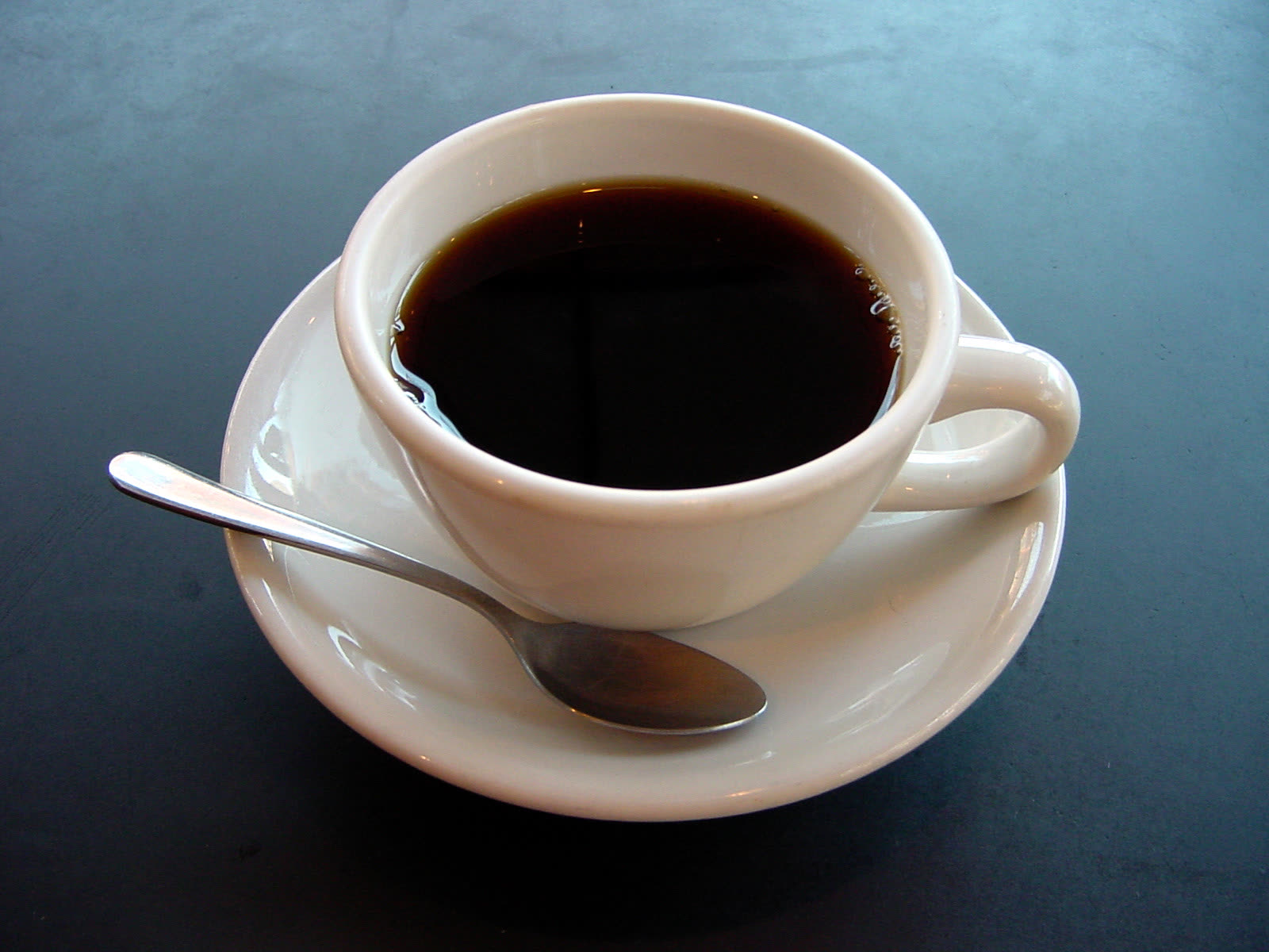 Taza de café negro sobre una mesa azul